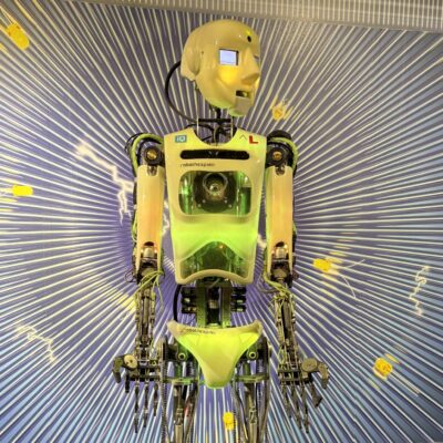 Ein humanoider Roboter mit durchsichtigem Brustkorb und neongrünen Teilen steht auf einem Podest, das vor einer grafischen Kulisse aufgebaut ist - ein auffälliges Highlight, das perfekt zu den Schlechtwettertipps Oberlausitz mit Teenagern passt.