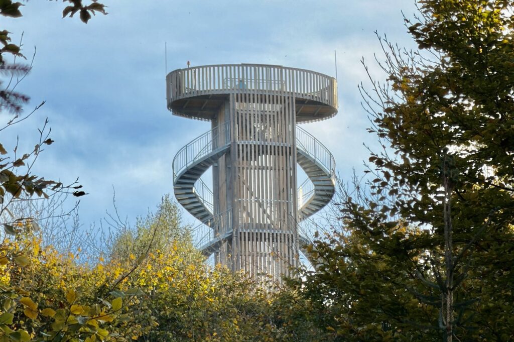 Ein hoher, runder neuer Aussichtsturm auf dem Jüttelsberg (Jitrovník) aus Holz und Metall mit einer Wendeltreppe, der sich über den Baumkronen erhebt.