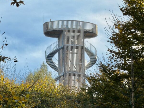 Ein hoher, runder neuer Aussichtsturm auf dem Jüttelsberg (Jitrovník) aus Holz und Metall mit einer Wendeltreppe, der sich über den Baumkronen erhebt.
