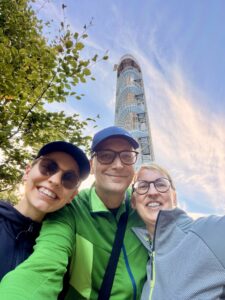 Wandernde vor dem neuen Aussichtsturm Jüttelsberg (Jitrovník) bei Schluckenau. Sie lächeln auf einem Selfie im Freien, im Hintergrund ist ein hoher, spiralförmiger Aussichtsturm auf dem Jüttelsberg (Jitrovník) zu sehen.