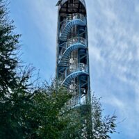 Hoher Aussichtsturm mit einer spiralförmigen Metalltreppe, von unten vor blauem Himmel gesehen.
